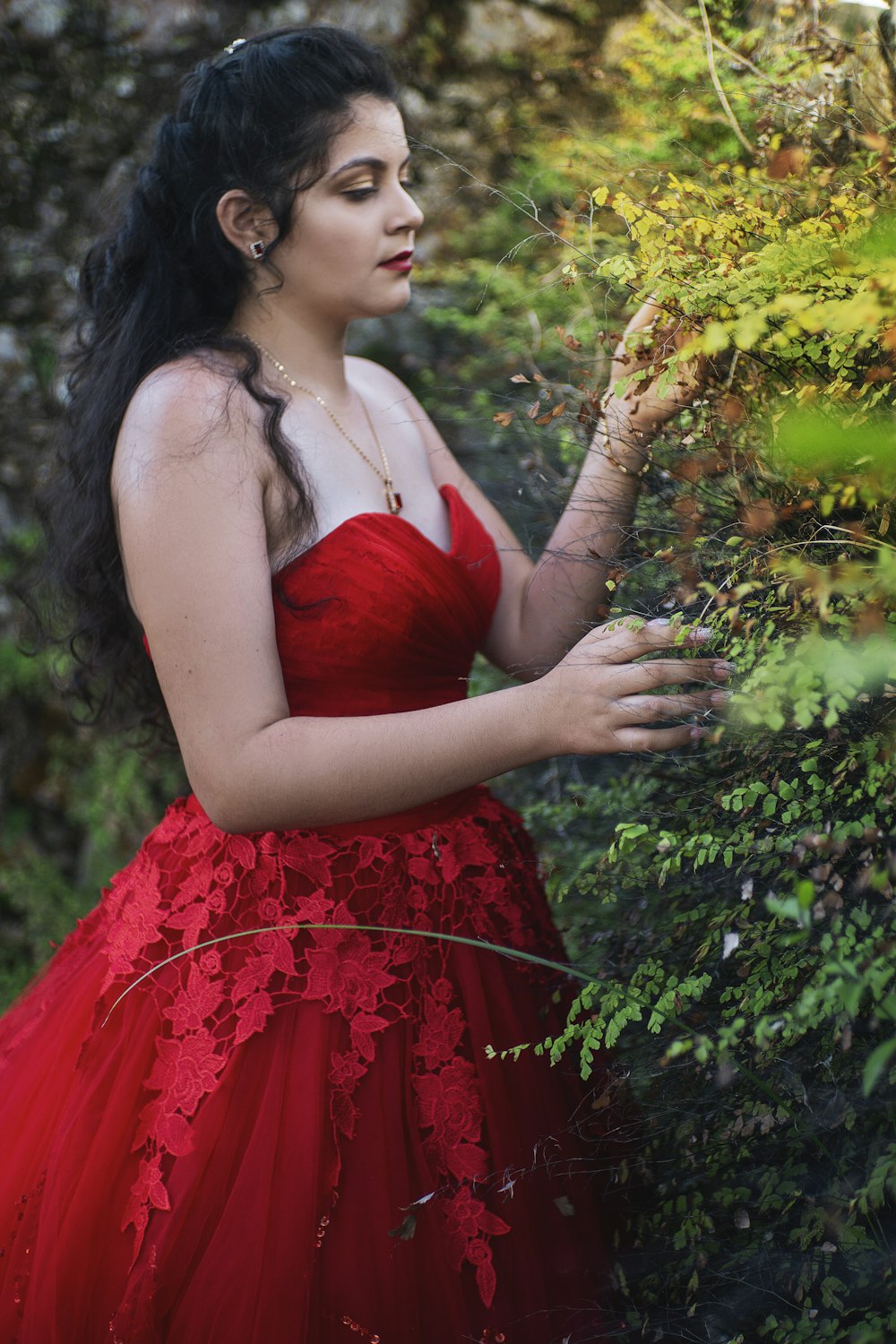 a woman in a red dress standing next to a bush