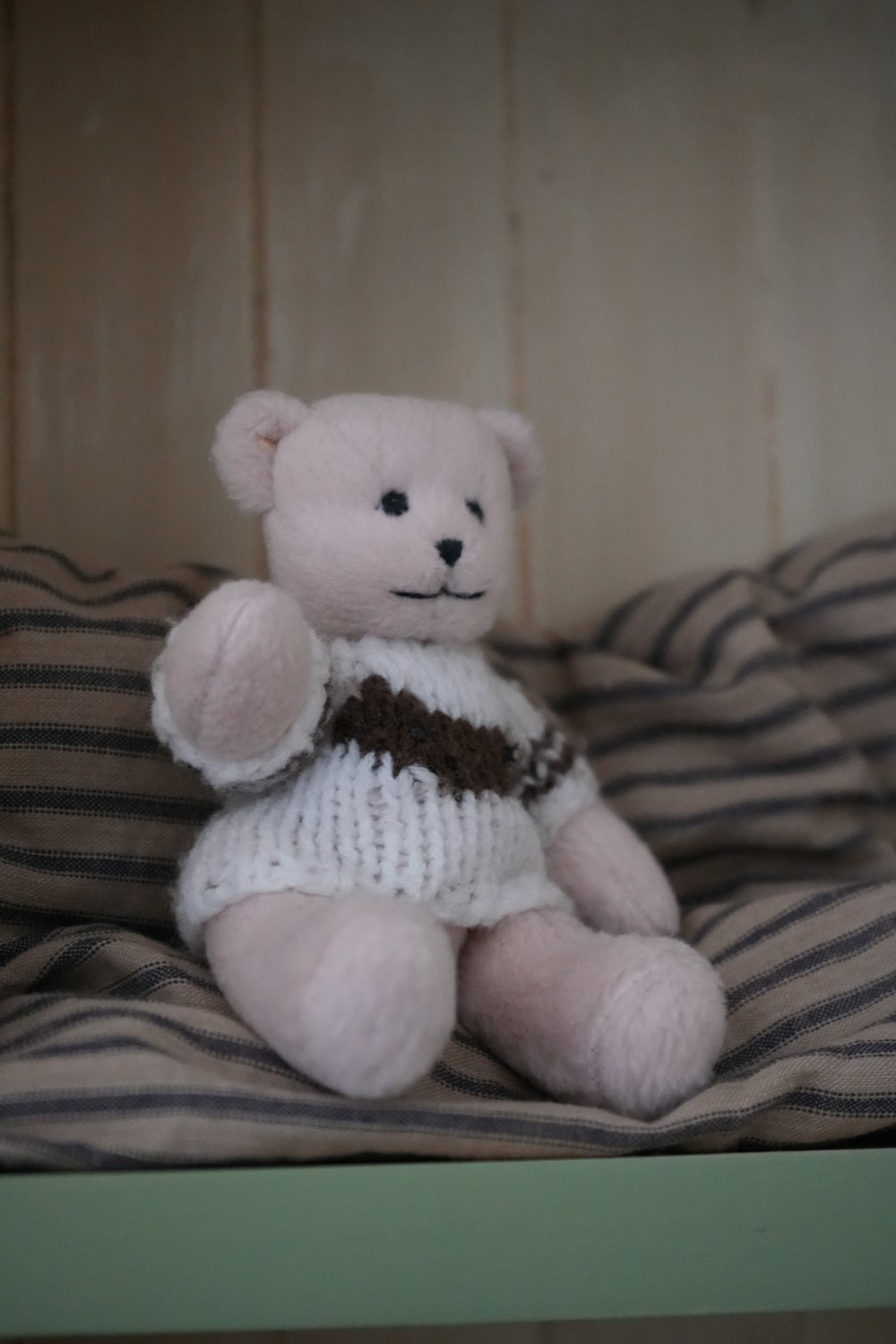 a teddy bear wearing a sweater sitting on a bed
