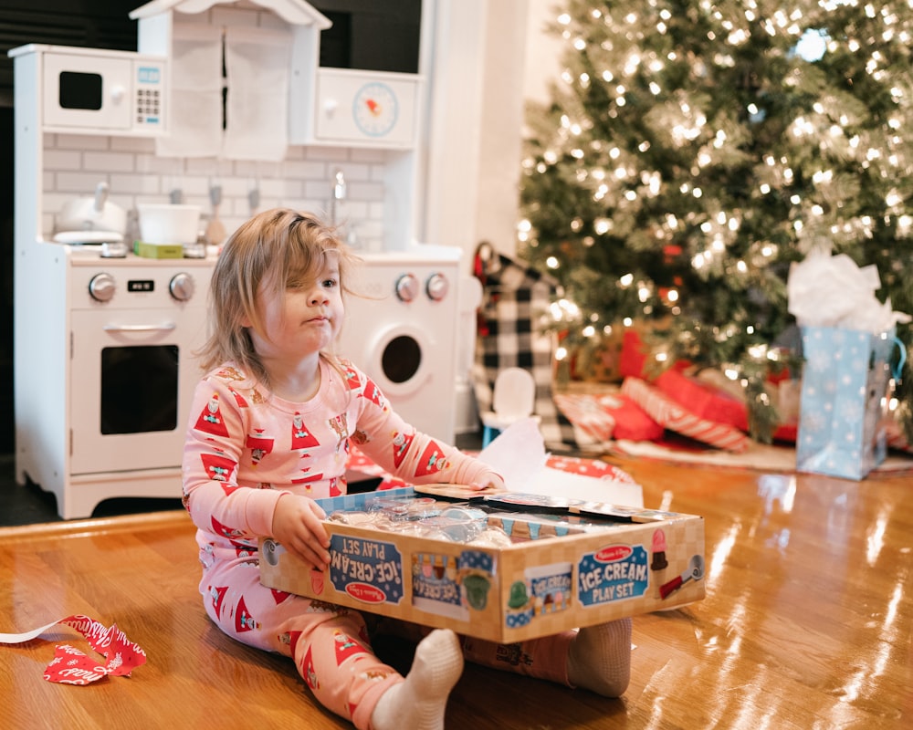 Une petite fille assise par terre devant un sapin de Noël