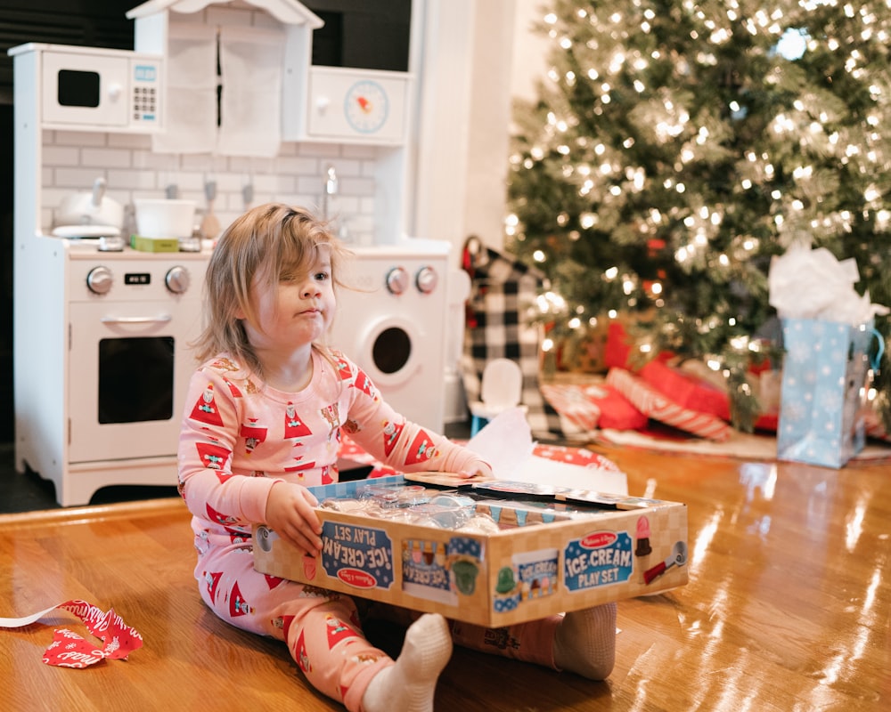 a little girl sitting on the floor in front of a christmas tree