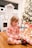 A small child in festive pajamas sits on a wooden floor, appearing to brush their teeth with a colorful toothbrush. In the background, there is a decorated Christmas tree and a play kitchen set.