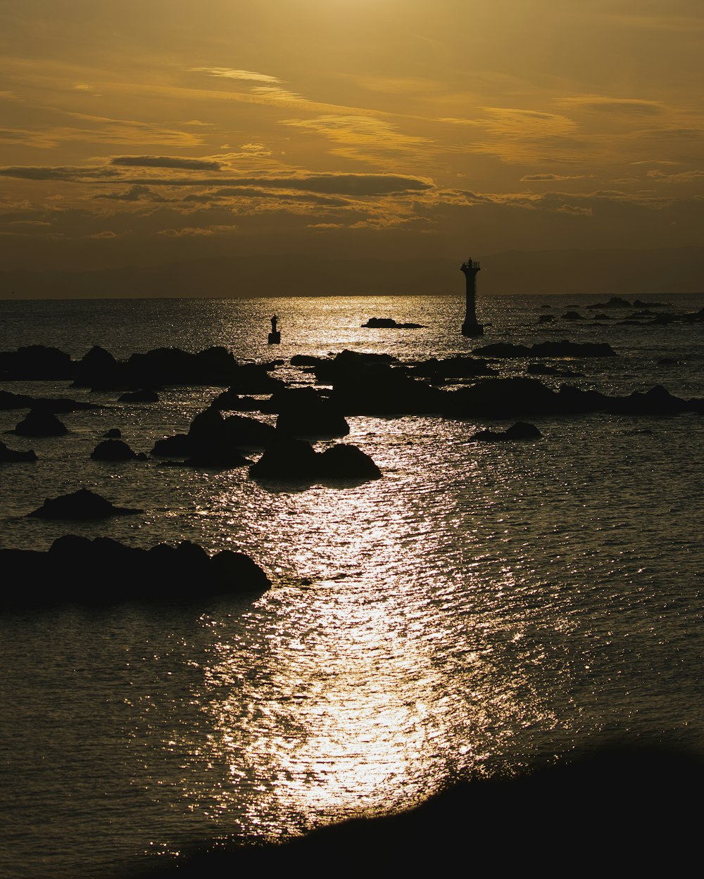 Une personne debout sur des rochers dans l’océan au coucher du soleil