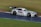 A sleek race car with a futuristic design is speeding along a wet track. The car is adorned with a number one and features various logos and decals. It has a large rear spoiler and is captured in motion, highlighting its dynamic capabilities.
