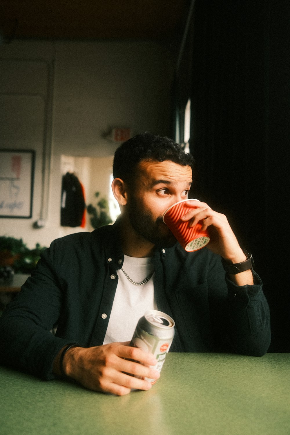 a man sitting at a table drinking from a can