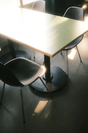 A sleek dining table set in a bright, minimalist room with sunlight casting soft shadows.