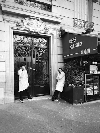 a couple of men standing outside of a pizza shop