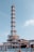 A large industrial structure with a tall metallic tower and multiple pipes and platforms, set against a clear blue sky. The structure appears complex, with interconnecting parts and support beams.