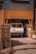 A white truck with an orange cab is parked inside an industrial building. The structure is made of corrugated metal sheets painted brown. Stacks of wooden pallets are on the left, and there is some machinery and large bags of materials on the right.