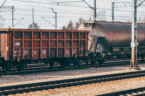 Freight train cars are stationed on railway tracks, with overhead electrical lines and pylons visible. The scene is clear, and the environment seems calm and industrial.