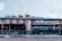 An industrial setting featuring large cylindrical storage tanks and freight train cars. The tanks are white with yellow access ladders and piping on top. The train cars have visible weathering, situated behind a metal fence. Overhead pipes run parallel to the tanks and ground.