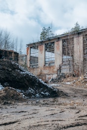 A misty abandoned industrial building surrounded by overgrown vegetation at dawn.