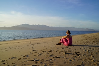 a woman in a pink dress sitting on a beach