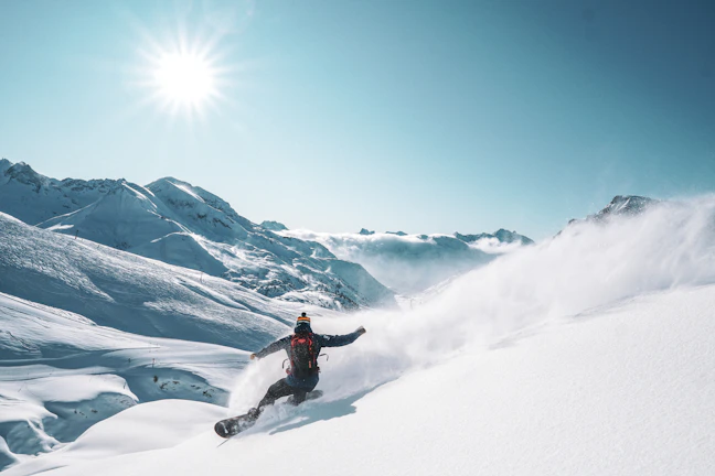 A snowboarder cruising down a powdery slope with a Triple Canber strapped securely, cans gleaming in the sun.