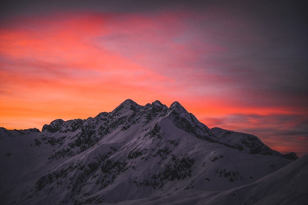 a mountain covered in snow under a pink sky
