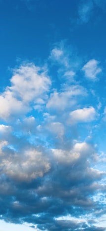 The image features a clear blue sky adorned with various fluffy white and gray clouds. The clouds range in size and shape, moving softly across the sky, suggesting a peaceful and calm weather condition.