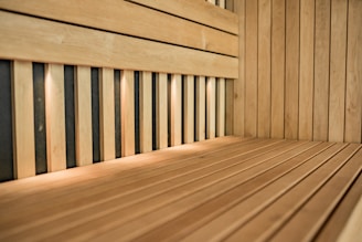 An interior of a wooden sauna featuring light wood panels and a bench. The space is lit by small recessed lights, casting a warm glow over the wood surfaces.