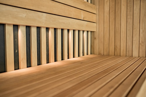 An interior of a wooden sauna featuring light wood panels and a bench. The space is lit by small recessed lights, casting a warm glow over the wood surfaces.