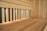 An interior of a wooden sauna featuring light wood panels and a bench. The space is lit by small recessed lights, casting a warm glow over the wood surfaces.