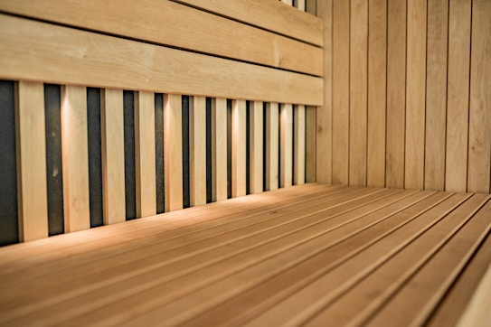 An interior of a wooden sauna featuring light wood panels and a bench. The space is lit by small recessed lights, casting a warm glow over the wood surfaces.