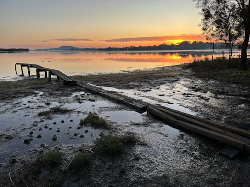 A serene sunrise casting golden light over a quiet lakeside dock.