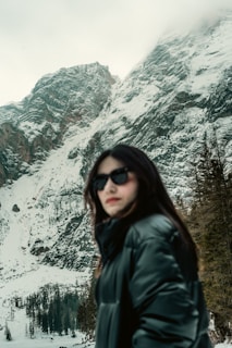 Man wearing a sleek black winter jacket standing against a snowy mountain backdrop.