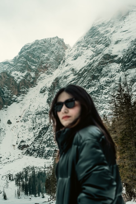 Man wearing a sleek black winter jacket standing against a snowy mountain backdrop.