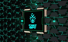 A stylized representation of a computer chip is integrated into a black and teal geometric background. The chip features a minimalist, futuristic face design along with the text 'CHAT GPT' in bold, glowing teal. The background consists of repeating black shapes outlined in teal, creating a high-tech, digital atmosphere.