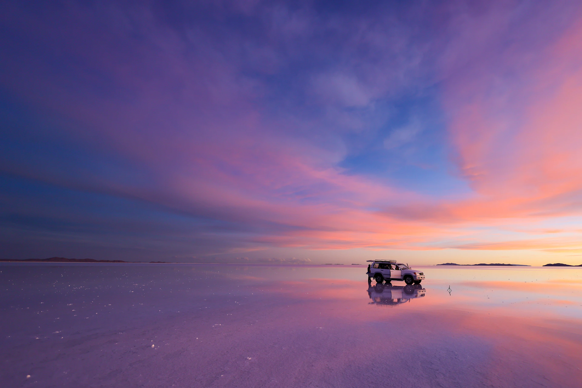 a car is parked on the beach at sunset