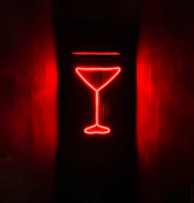 A glowing cocktail glass illuminated by golden neon lights on a sleek black bar.