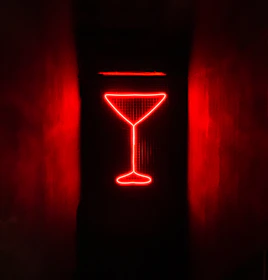 A glowing cocktail glass illuminated by golden neon lights on a sleek black bar.