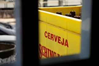 A bright yellow crate with empty brown glass bottles is partially visible through a window. The word 'CERVEJA' is printed in bold red letters on the side of the crate.