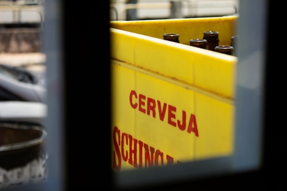 A bright yellow crate with empty brown glass bottles is partially visible through a window. The word 'CERVEJA' is printed in bold red letters on the side of the crate.