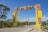 An entrance archway with the words 'Bienvenidos a Jimaní' stands over a road. The structure features bold geometric shapes in yellow and red-orange. Surrounding the road are trees, and in the background, mountains are visible under a clear blue sky.