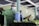 A person in a green uniform and hairnet is wearing a face mask while operating a sprayer. They appear to be working in a facility with green walls and are spraying a row of bananas.