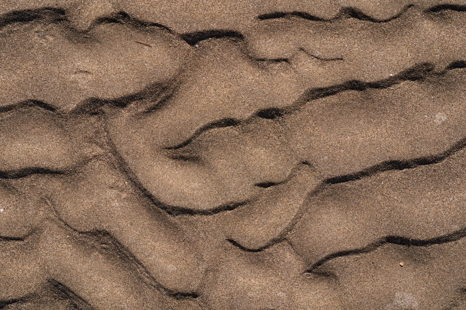 Close-up view of sandy beach with rippled texture and light brown hue from above