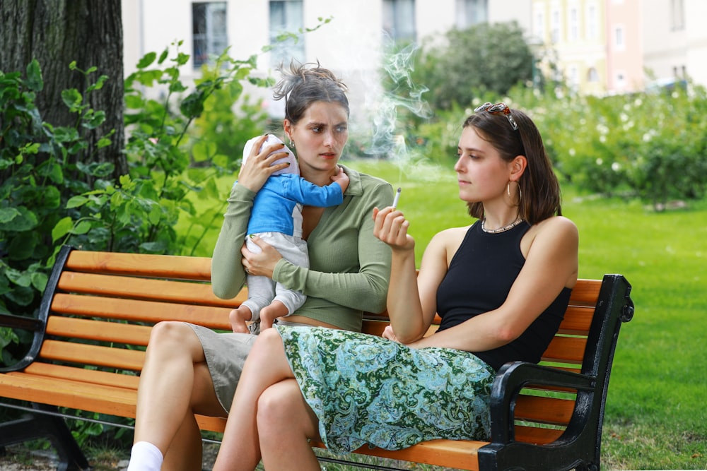 two women sitting on a park bench smoking a cigarette