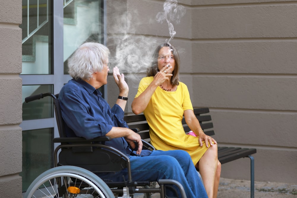 a woman smoking a cigarette next to a man in a wheelchair
