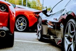 Two luxury sports cars are parked closely together on a paved surface, showcasing their sleek rear and side bodies. The focus is on their glossy finishes and distinct tire designs, reflecting an aura of elegance and high-performance engineering.
