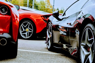 Two luxury sports cars are parked closely together on a paved surface, showcasing their sleek rear and side bodies. The focus is on their glossy finishes and distinct tire designs, reflecting an aura of elegance and high-performance engineering.