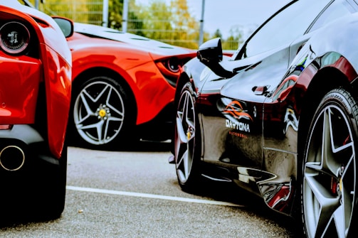 Two luxury sports cars are parked closely together on a paved surface, showcasing their sleek rear and side bodies. The focus is on their glossy finishes and distinct tire designs, reflecting an aura of elegance and high-performance engineering.