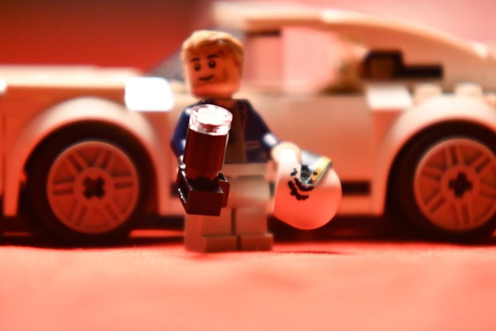 a lego man holding a beer next to a toy car