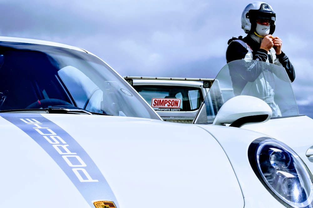 a man in a helmet standing next to a white sports car