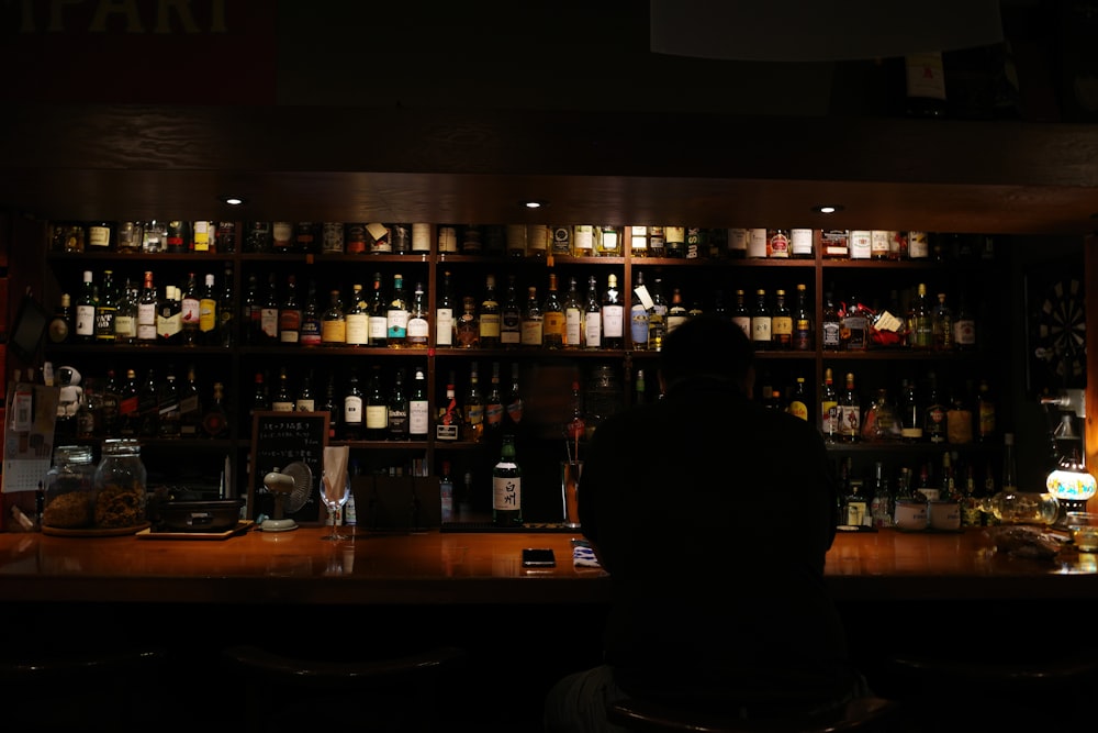 Un hombre sentado en un bar con muchas botellas detrás de él