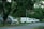Several parked vehicles, including an ambulance, are lined up on the side of a road surrounded by lush greenery and trees. The vehicles appear to be stationary with some signs of wear.