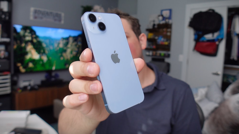 a man holding up an iphone in front of a tv
