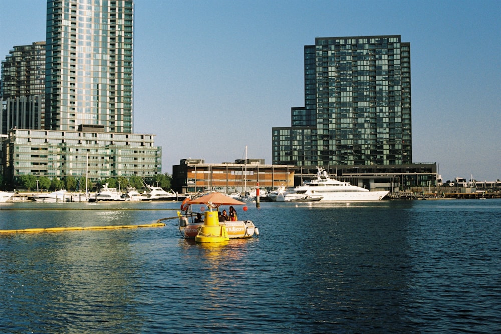 a yellow boat floating on top of a lake next to tall buildings