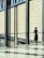A person in a black outfit stands alone in a modern, spacious, and well-lit architectural space. Large glass windows and a wall with a geometric pattern dominate the scene. The person appears to be deep in thought or contemplation.