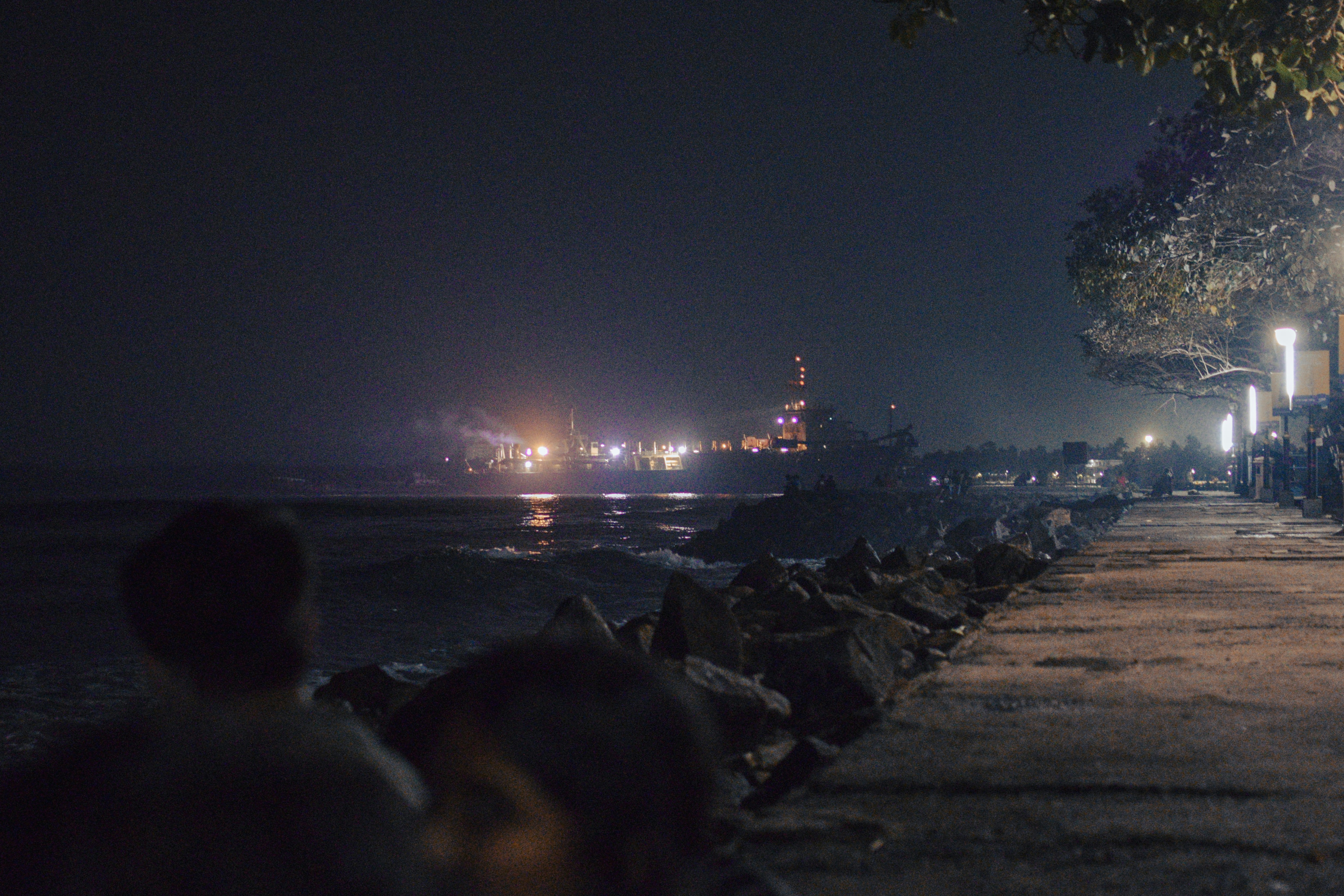 An atmospheric shot of a narrow, dimly lit lane in Fort Kochi at dusk, with old colonial buildings on either side and a faint glow from a street lamp or lantern.