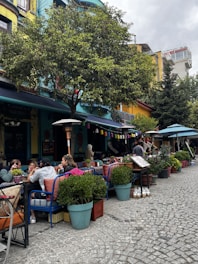 Outdoor coffee pavilion with hanging lanterns and patrons enjoying drinks under leafy trees.