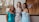 Three women in elegant evening gowns are smiling and posing together in front of a window. One wears a turquoise off-shoulder dress, the second wears a sequined gown with diagonal stripes, and the third wears a light blue dress with floral lace details. The background shows an indoor setting with a hint of wedding dresses and a sign.